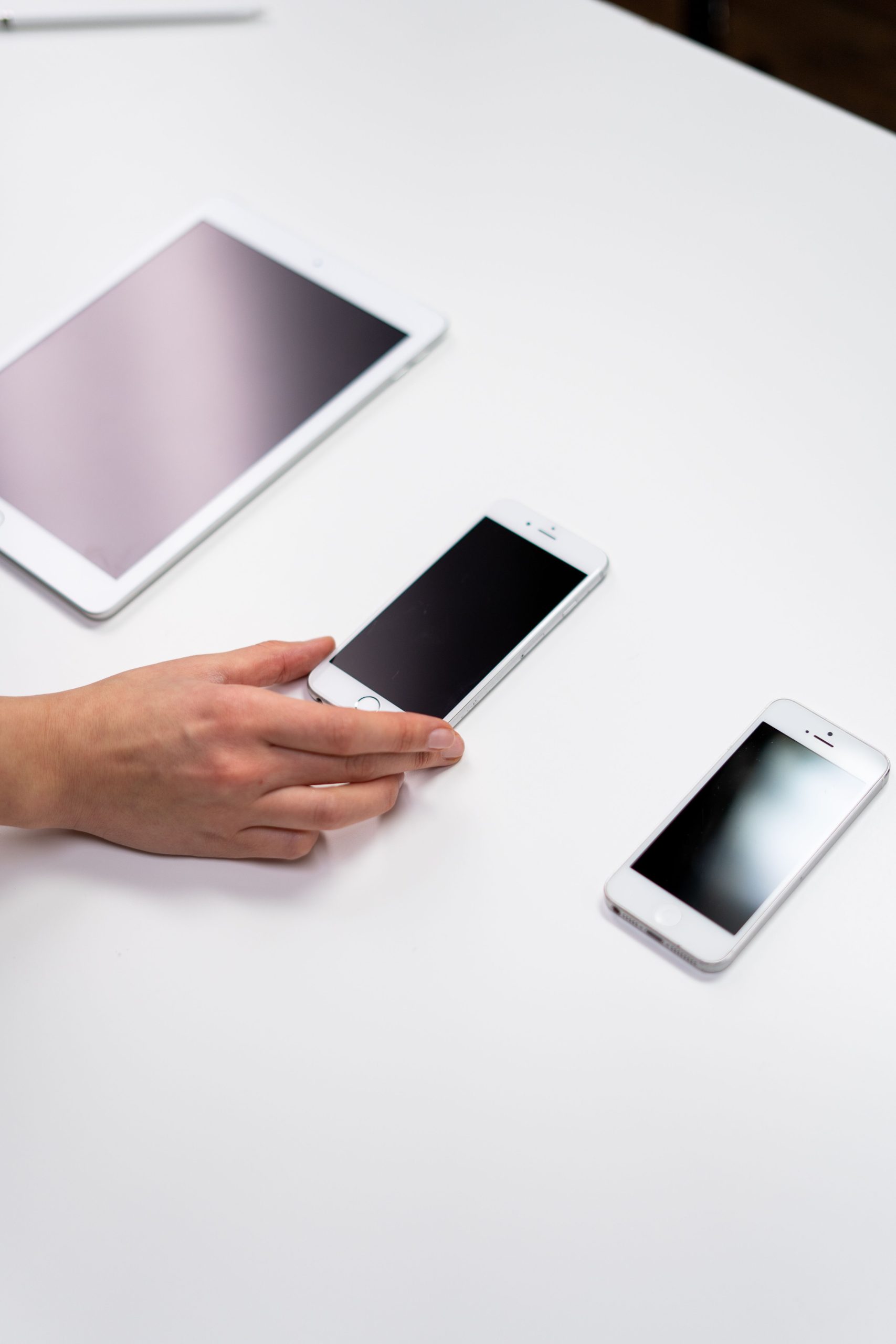 Top view of a minimalist setup featuring a tablet and smartphones on a white surface.
